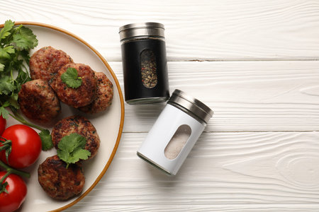 Salt and pepper shakers, meatballs on white wooden table, flat lay. Space for text