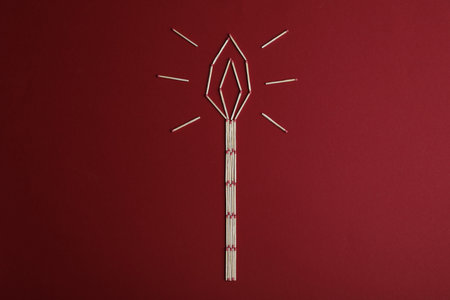 Burning candle made of matches on red background, top view