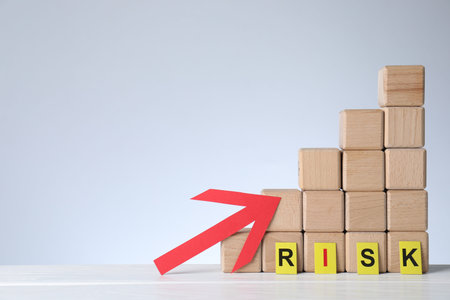 Word Risk, red arrow and stacked cubes on white wooden table against light background, space for...