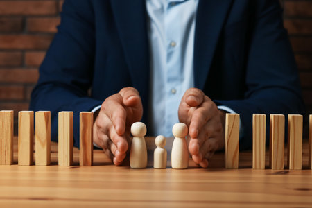 Risk. Man protecting human figures from domino effect at wooden desk, closeupの写真素材