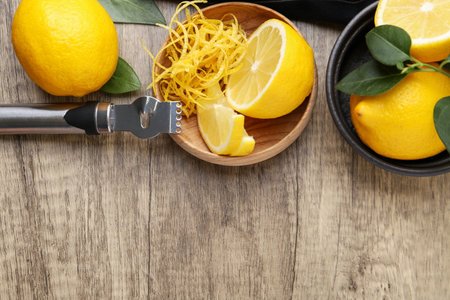 Lemon zest in bowl, fresh fruits, zester tool and green leaves on wooden table, flat lay. Space for...