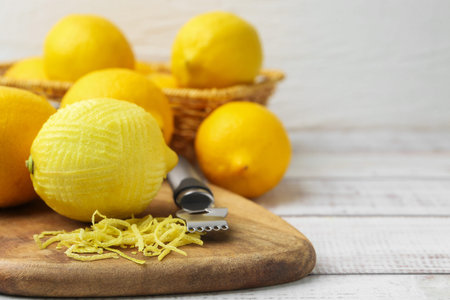 Lemon zest, fresh fruits and zester tool on light wooden table, closeup