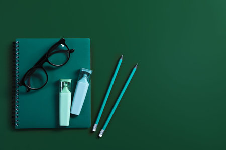Notebook, stationery and glasses on green background, flat lay. Space for text