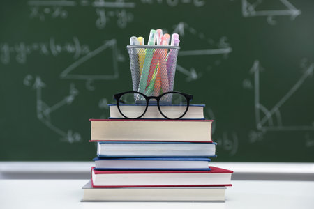 Happy teacher's day. Books, glasses and stationery on white table against chalkboard