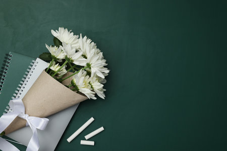 Happy Teacher's Day. Notebooks, flowers and pieces of chalk on chalkboard, flat lay. Space for textの写真素材