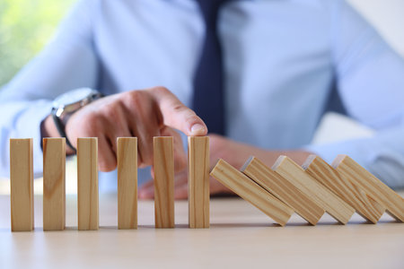 Risk. Man stopping domino effect at table, closeupの写真素材
