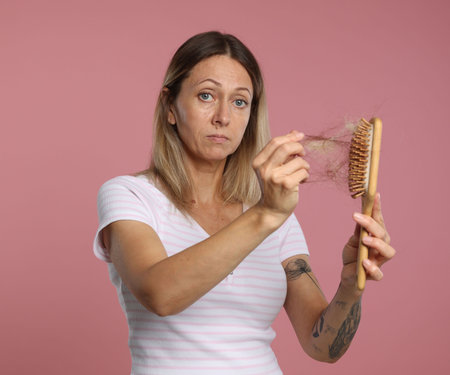 Alopecia problem. Woman taking her lost hair from brush on pink backgroundの写真素材