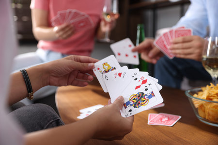 Friends playing cards at wooden table indoors, selective focus