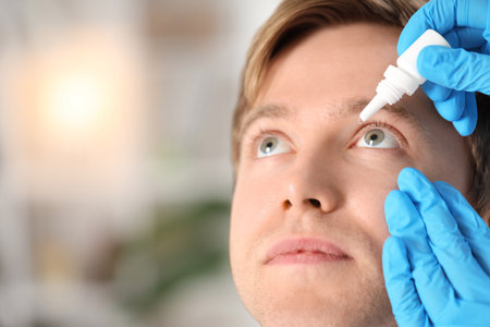 Doctor applying medical drops into man's eye indoors, closeup. Space for textの写真素材