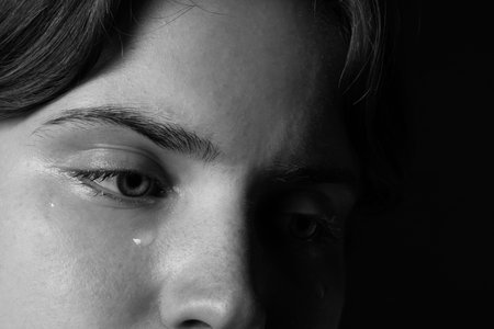 Sad woman crying on dark background, closeup. Black and white effect