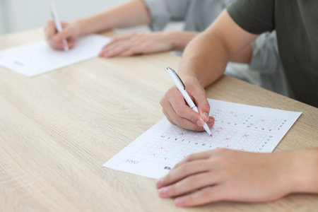 Students filling out answer sheet at wooden table indoors, closeup. Taking examの写真素材