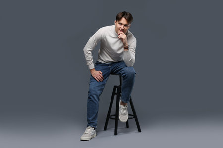 Man in stylish jeans on stool against gray backgroundの写真素材