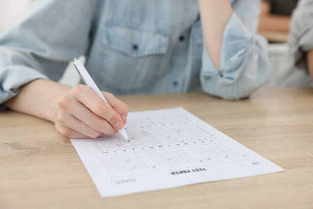 Student filling out answer sheet at wooden table indoors, closeup. Taking examの写真素材