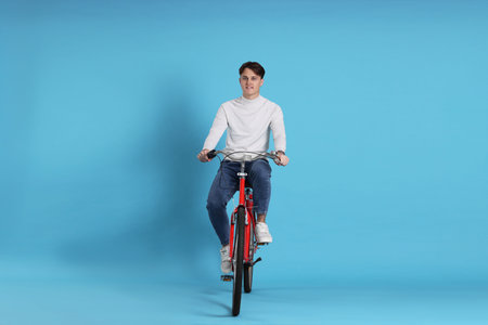 Handsome man riding red bicycle on light blue background