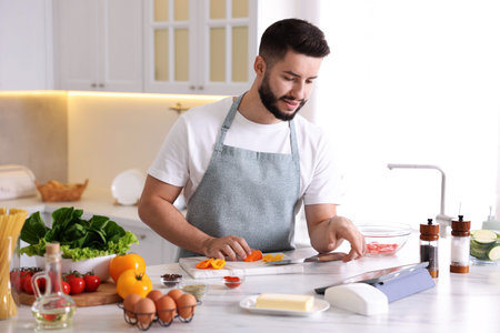Young man looking at recipe on tablet while cooking at table in kitchen