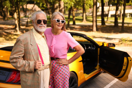 Stylish senior couple in sunglasses near modern cabriolet outdoors