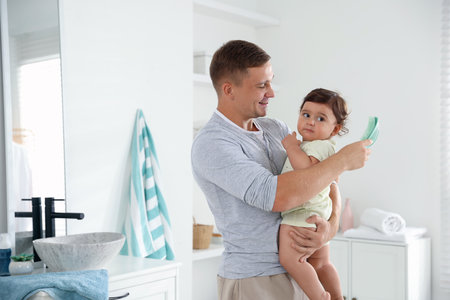 Father brushing his baby's hair in bathroom, space for textの写真素材