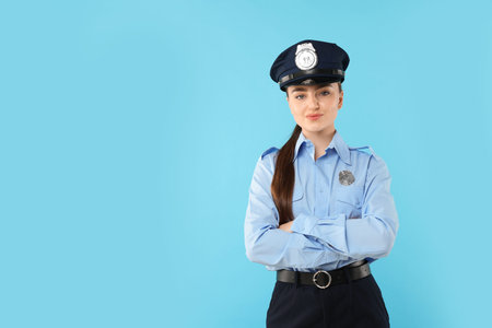 Young policewoman in uniform on light blue background, space for text