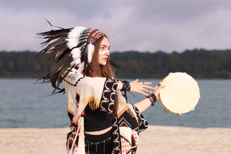 Beautiful shaman woman in native American Indian headdress with face painting and tambourine...