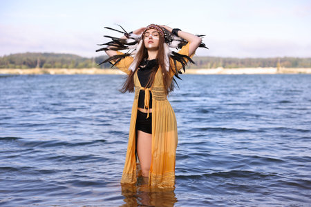 Beautiful shaman woman in native American Indian headdress with face painting in river water