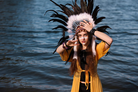Beautiful shaman woman in native American Indian headdress with face painting in river water.