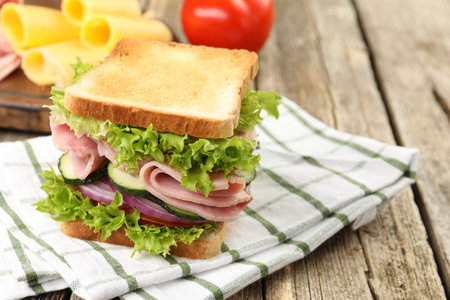 Tasty sandwich with ham and vegetables on wooden table, closeup. Space for textの写真素材