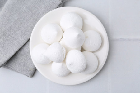 Delicious meringue cookies on white tiled table, top view
