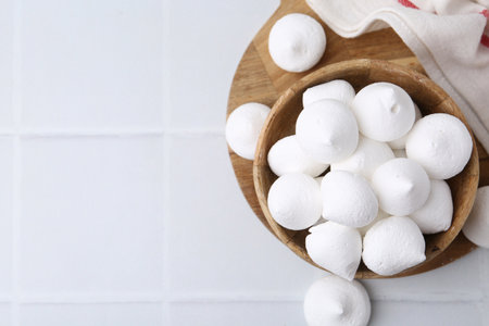 Delicious meringue cookies in bowl on white tiled table, top view. Space for textの写真素材