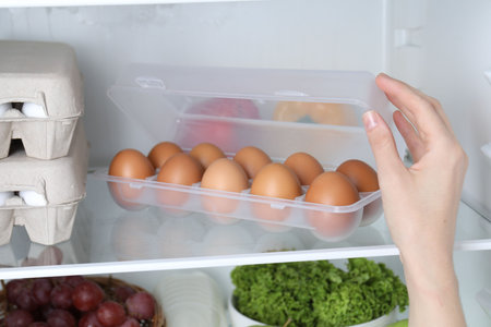 Woman opening container with raw chicken eggs in refrigerator, closeup