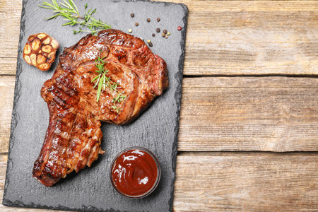 Delicious grilled beef steak with herbs, spices and ketchup on wooden table, flat lay. Space for textの写真素材