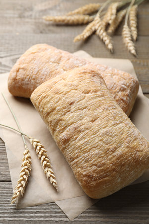Freshly baked ciabattas and wheat ears on wooden table, closeupの写真素材