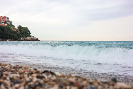 Beautiful view of wavy sea and pebbles on beach, selective focus