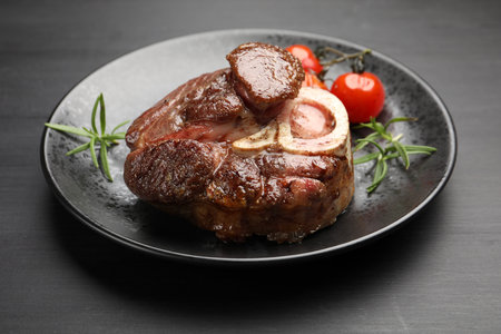 Tasty grilled beef steak served with rosemary, sauce and tomatoes on black wooden tableの写真素材