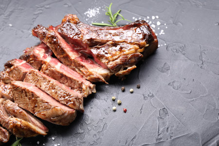 Tasty cut beef steak, salt, peppercorns and rosemary on black table, closeup. Space for textの写真素材