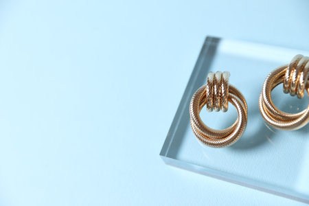 Beautiful gold earrings on light blue background, closeup. Space for textの写真素材
