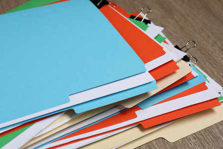 Many documents in folders with binder clips on wooden table, closeup