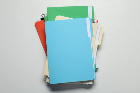 Many documents in folders with binder clips on light gray background, top view