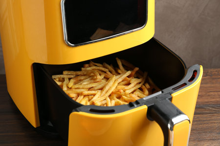Air fryer container with cooked French fries on wooden table, closeupの写真素材