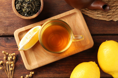 Aromatic tea in cup with lemons, dry leaves and teapot on wooden table, flat layの写真素材