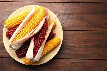 Red and yellow corn cobs on wooden table, top view. Space for text