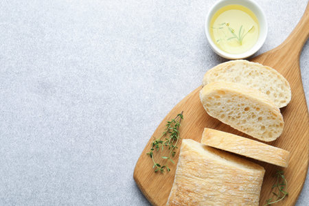 Fresh crispy bread, oil and herbs on gray table, flat lay. Space for text
