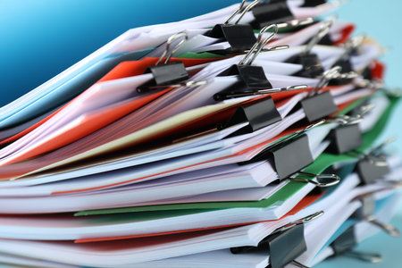 Many folders with documents and binder clips on light blue background, closeup