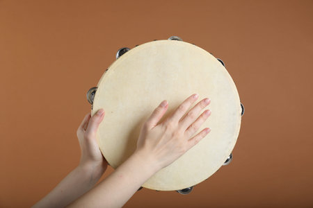 Woman playing tambourine on brown background, closeupの写真素材