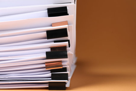 Many documents with binder clips on brown background, closeup. Space for text