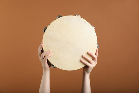 Woman playing tambourine on brown background, closeupの写真素材
