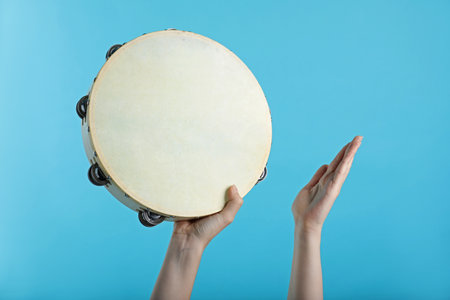 Woman playing tambourine on light blue background, closeupの写真素材