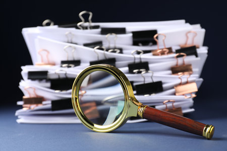 Magnifying glass and many documents with binder clips on dark background, closeupの写真素材