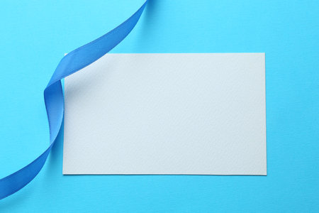 Beautiful ribbon and blank card on light blue background, flat layの写真素材