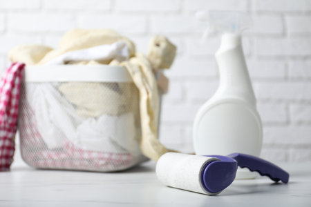 Lint roller, bottle of cleaning product and clothes on white marble table against brick wall, closeup. Space for textの写真素材