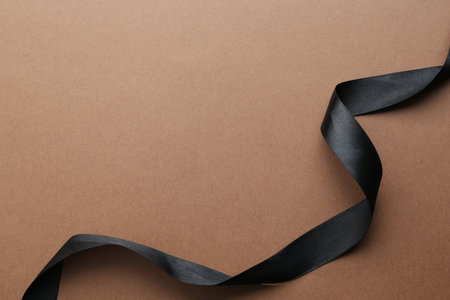 Beautiful black ribbon on light brown background, top view. Space for textの写真素材